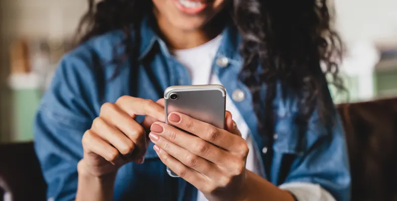 Smiling African woman at home using her smartphone with one hand on the screen 