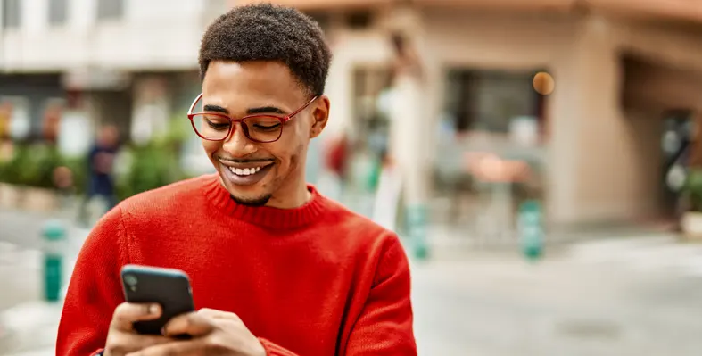 African American man outdoors, typing on smartphone