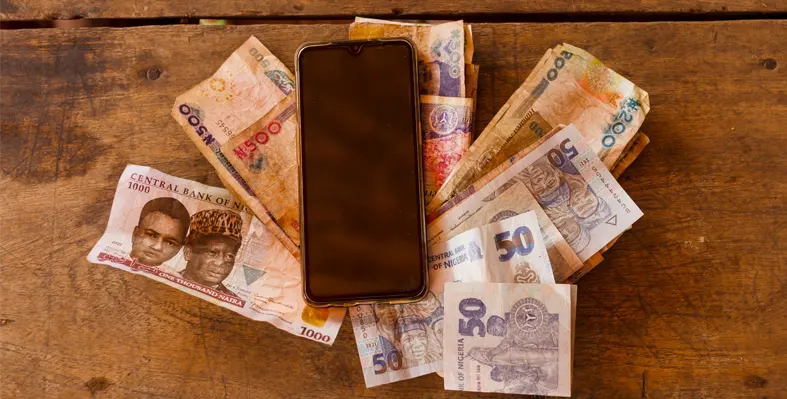 Image of a mobile phone on top colorful African currency note