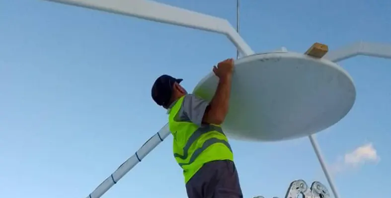 A man on a ladder fixing a satellite